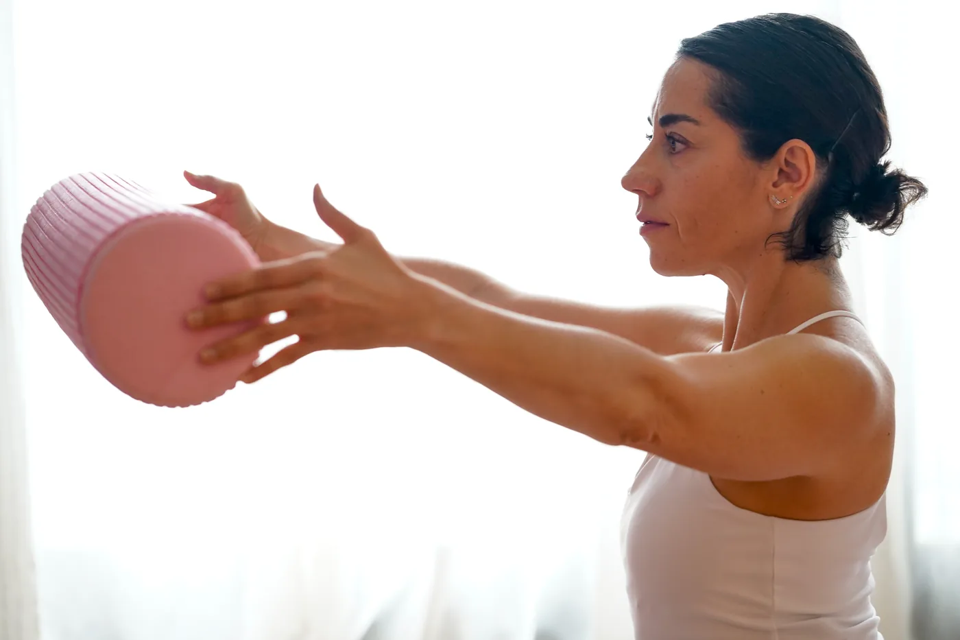 Belén sentada de perfil, con los brazos extendidos sosteniendo un rodillo de Pilates