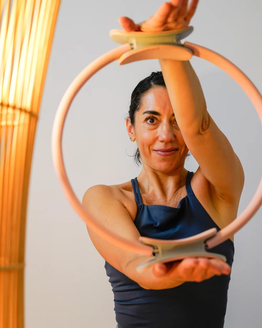 Belén con los brazos en alto, sosteniendo el aro de Pilates por encima de la cabeza